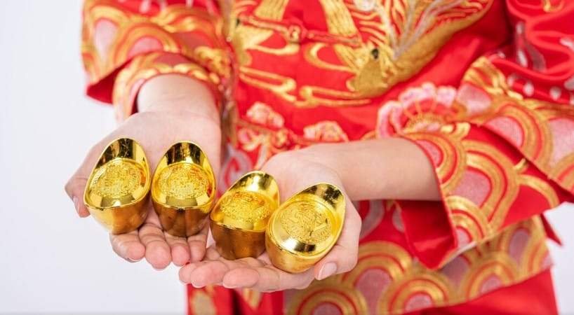 sebuah tangan menggunakan baju berwarna merah dan emas sedang membawa barang berwarna emas, salah satu arti warna merah dan emas dalam imlek