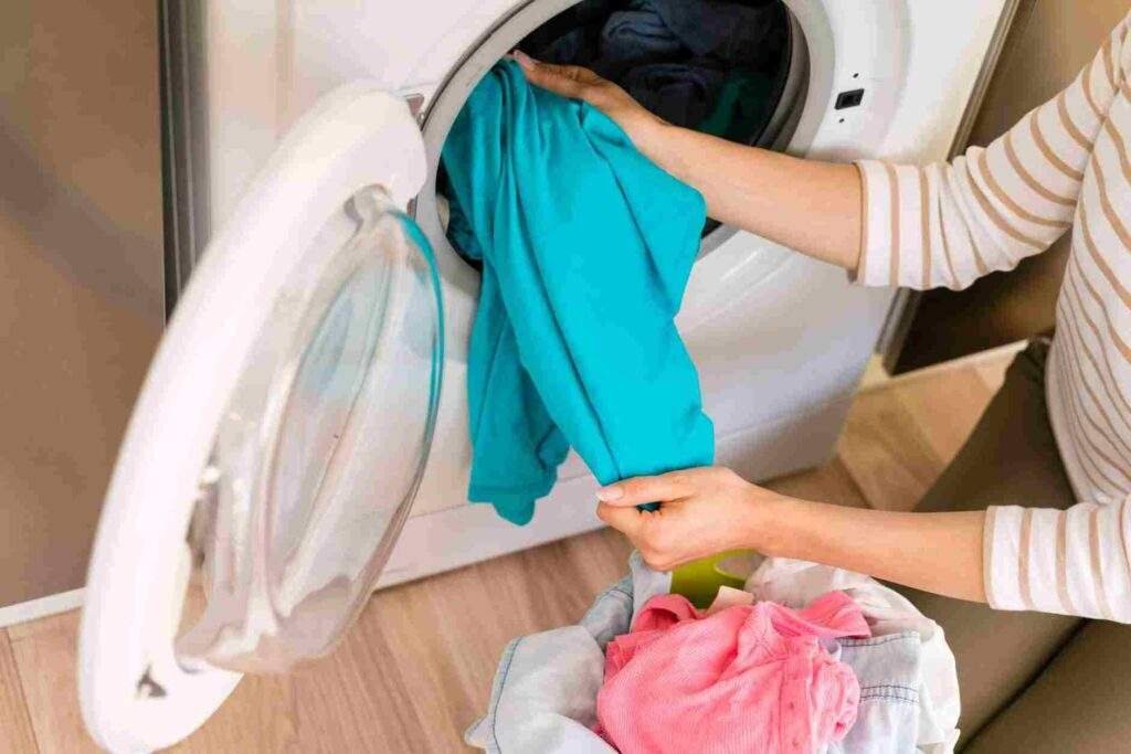 Tangan memasukkan pakaian ke mesin cuci sebagai langkah dari 10 cara mencuci baju di mesin cuci agar bersih dan wangi