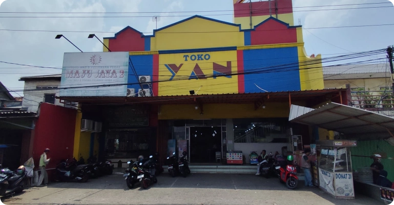 Mitra 1 Fasad Toko Yan di lokasi ramai, dikelilingi area parkir dan kendaraan pengunjung yang menunjukkan tingginya trafik.