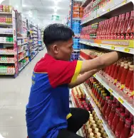 Karyawan Toko Yan sedang merapikan botol saus di rak supermarket agar tampilan lebih rapi.