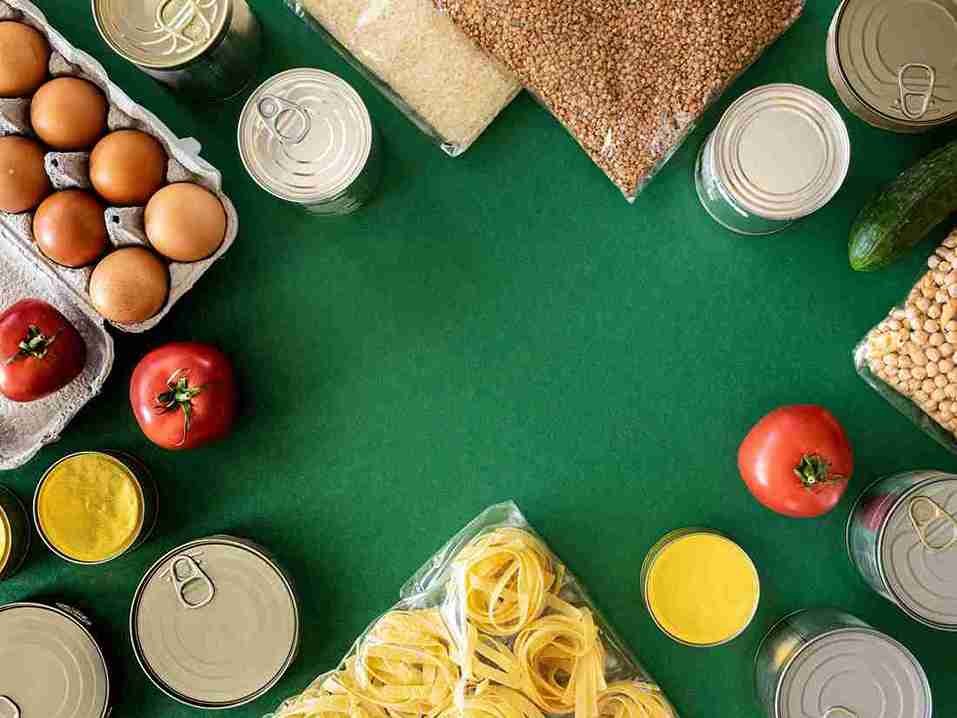 Sembako Apa Saja yang Wajib Ada di Rumah? Daftar Jenis Sembako 1 Beragam bahan sembako tersusun di atas meja hijau, termasuk telur, tomat, pasta, kacang-kacangan, mentimun, beras, dan makanan kaleng.