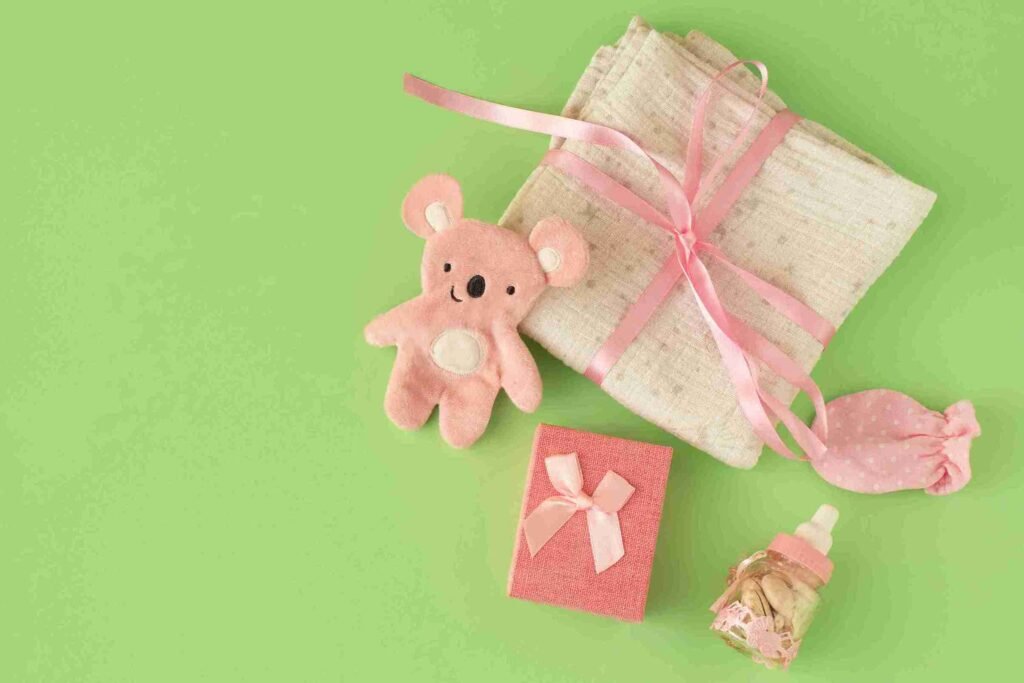 Set kado bayi dengan boneka beruang pink, kotak kado, kantong polka dot, dan botol bayi, di latar belakang hijau